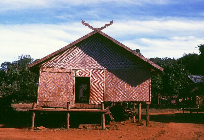 A wooden house on stilts with walls woven in a diamond pattern and a peaked roof.