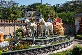 Painted statues of horses and figures in a raised garden bed within a temple courtyard.