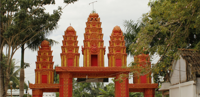 A red gateway with three pointed towers between trees.