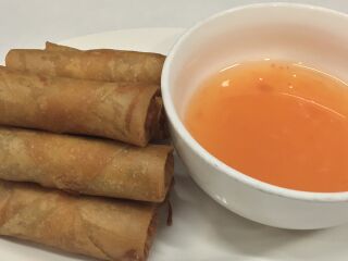 Fried spring rolls on a plate beside a bowl of orange dipping sauce.