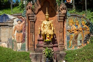 A carved stone monument with a central seated gilded figure, flanked by relief panels of standing figures.
