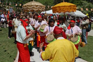 A crowd outdoors under parasols watching drummers in red and yellow clothes play during a festival.