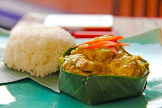 A banana-leaf cup of fish amok topped with red chilli strips beside a mound of white rice.