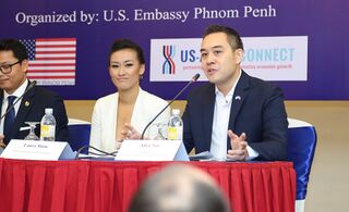 Panellists at a table with a red cloth, a woman in white beside a man speaking into a microphone.
