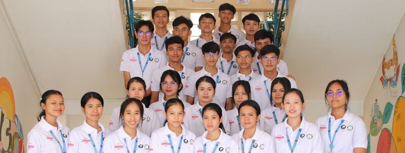 A large group of young adults in white uniform shirts and lanyards stand on a staircase.