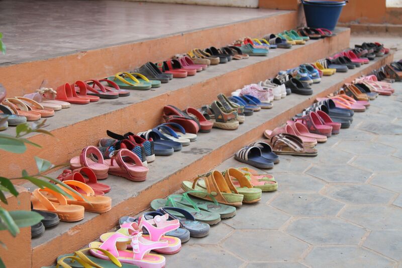 Rows of colorful children's sandals and flip-flops lined up neatly on tiered concrete steps.