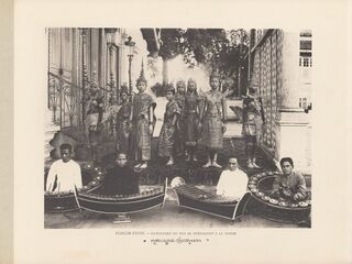 An old photograph of costumed dancers standing behind seated musicians with xylophones and gong chimes.
