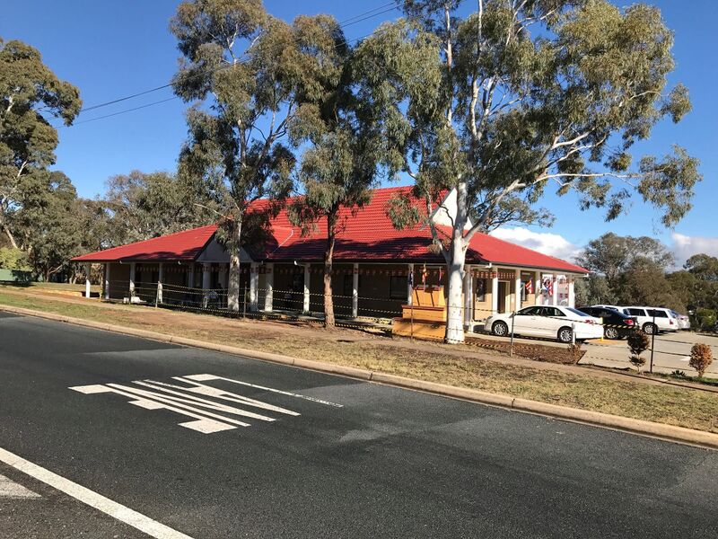 A long single-story building with a red roof and veranda among tall gum trees, seen across a road.