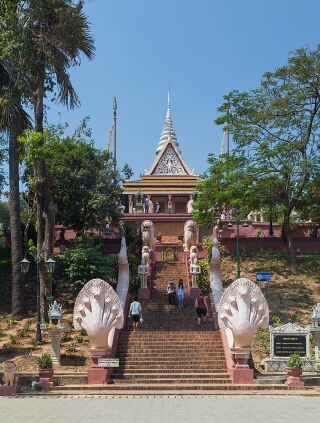 A wide stairway climbing a wooded hill toward a temple, its balustrades ending in large many-headed serpent sculptures.