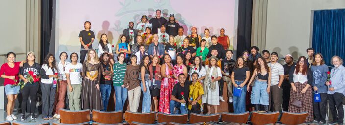 About fifty filmmakers, organizers and guests pose on the Art Theatre stage in front of the screen, many holding red roses, above rows of empty seats.