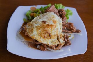 Stir-fried beef and onions with a runny fried egg on top and fresh salad leaves on a white plate.