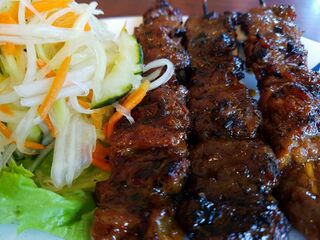 Charred beef skewers on a plate beside shredded pickled carrot and daikon and lettuce.