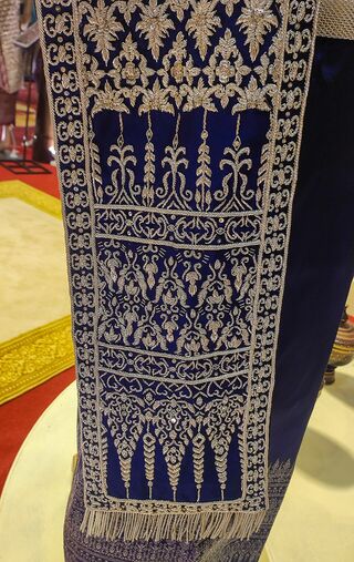 Gold embroidery of flowers and spires on a dark blue sbai, ending in a fringe.