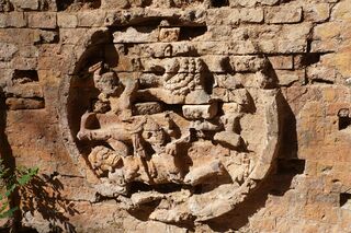 A round brick relief showing two small figures struggling with a lion.