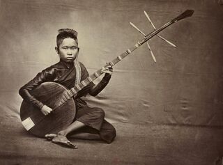 A sepia photograph of a young musician kneeling and holding a long-necked lute across the lap.