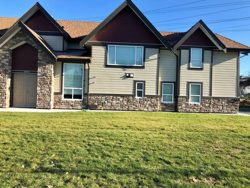 A two-story house with stone and siding walls behind a wide lawn.