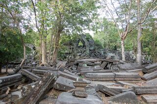Scattered stone beams and blocks on the forest floor, with a ruined doorway in the distance.